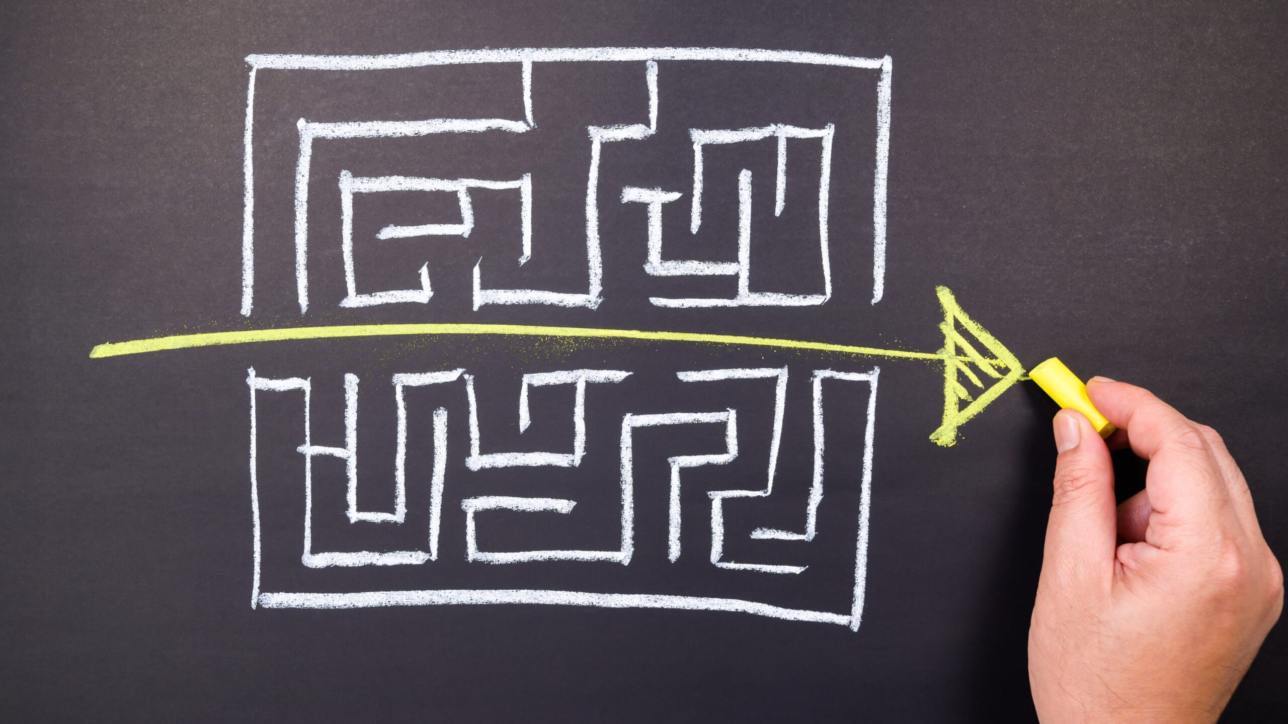 A maze is hand-drawn on a chalkboard, with a straight line running from one side to the other.