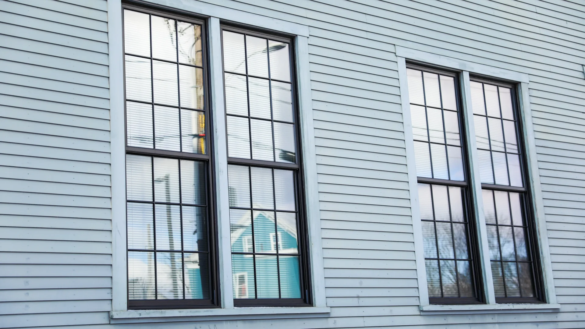 Four large vertical windows with black frames on home with pale siding